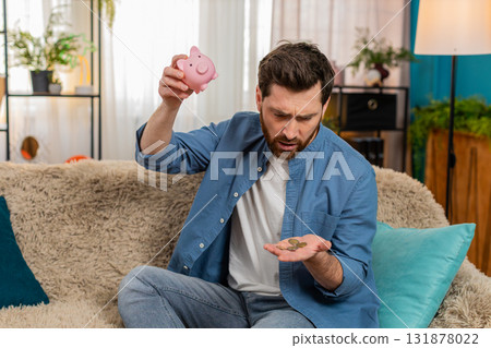 Man shaking piggy bank, counting collected coins, saving money, checking personal finances at home 131878022