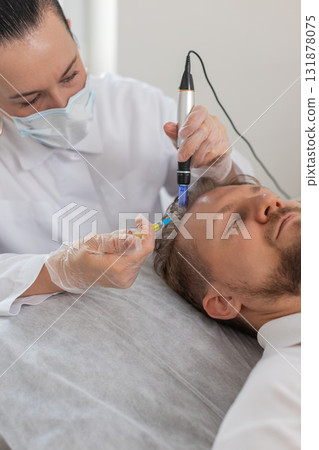 Trichologist doing man hair regeneration procedure dermapen microneedling vitamin exosomes injection Trichologist doing man hair regeneration procedure dermapen microneedling vitamin exosomes injection 131878075