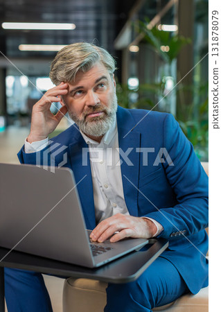 Bored sleepy mature Caucasian businessman working on laptop computer sitting in modern office lobby Bored sleepy mature Caucasian businessman working on laptop computer sitting in modern office lobby 131878079