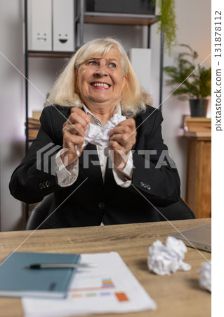 Angry senior businesswoman grandmother throwing crumpled paper while working at home office table 131878112
