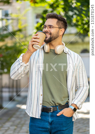 Happy Caucasian young man tourist in glasses enjoying morning coffee hot drink on city street Happy Caucasian young man tourist in glasses enjoying morning coffee hot drink on city street 131878145