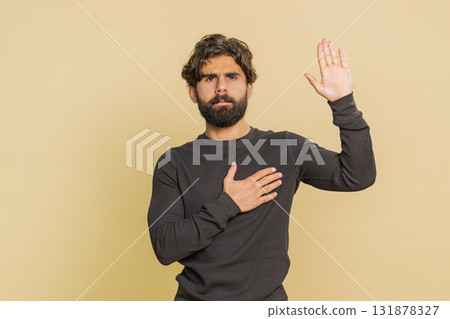 Sincere responsible man raising hand to take oath, promising to be honest against beige background 131878327
