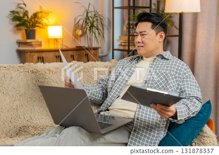 Stressed man freelancer feeling worried about financial problem doing paperwork sitting on sofa Stressed man freelancer feeling worried about financial problem doing paperwork sitting on sofa 131878337