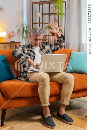 Displeased man use laptop surprised by bad news, virus error, game fail, lottery results at home 131878356