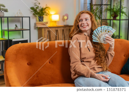 Successful rich young Caucasian woman holding euro bill money fan sitting on sofa couch at home Successful rich young Caucasian woman holding euro bill money fan sitting on sofa couch at home 131878371