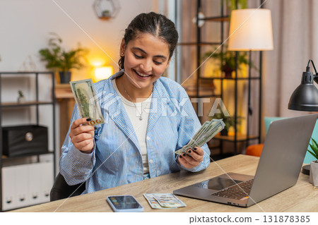 Happy rich Indian freelancer counting money cash using smartphone calculator app at home office desk 131878385