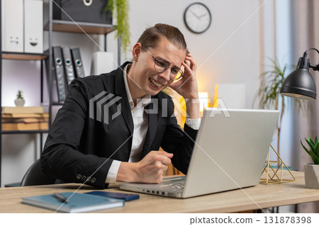 Sad businessman using laptop loses becoming surprised sudden lottery results at home office desk Sad businessman using laptop loses becoming surprised sudden lottery results at home office desk 131878398