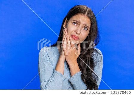 Young woman touching cheek, closing eyes with expression of terrible suffer from painful toothache Young woman touching cheek, closing eyes with expression of terrible suffer from painful toothache 131878400