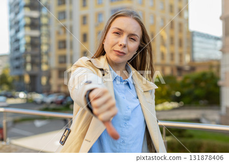 Upset mature Caucasian woman showing thumb down expressing discontent on downtown city street 131878406