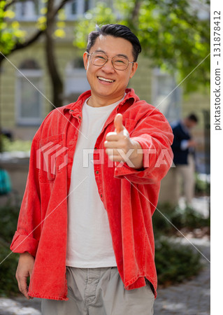 Happy Asian man showing thumbs up like sign positive something good positive feedback in city street Happy Asian man showing thumbs up like sign positive something good positive feedback in city street 131878412