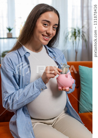 Pregnant woman inserting banknote money cash dollar in piggybank saving for baby's future needs 131878416