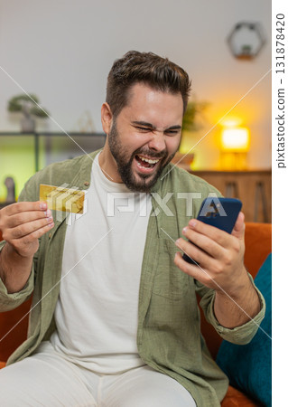 Angry stressed man trying to pay online shopping with smartphone blocked credit card on sofa at home Angry stressed man trying to pay online shopping with smartphone blocked credit card on sofa at home 131878420