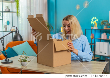 Happy blond businesswoman unpacking opening delivery parcel box purchase sits at desk in apartment 131878453