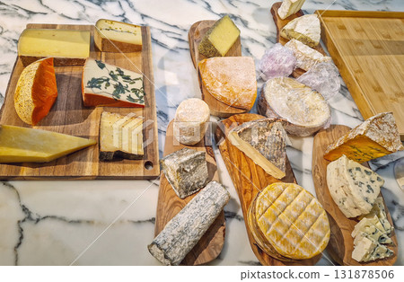 A generous variety of artisan cheeses on wooden cutting boards and bamboo trays. The diverse selection includes hard, soft, blue, and aged assortment of cheese on a white marble countertop A generous variety of artisan cheeses on wooden cutting boards and bamboo trays. The diverse selection includes hard, soft, blue, and aged assortment of cheese on a white marble countertop 131878506