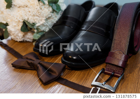 Wedding Shoes and Accessories Still Life: Dark Brown Leather Loafers, Bow Tie, Belt, and White Bouquet on Wood Surface Wedding Shoes and Accessories Still Life: Dark Brown Leather Loafers, Bow Tie, Belt, and White Bouquet on Wood Surface 131878575