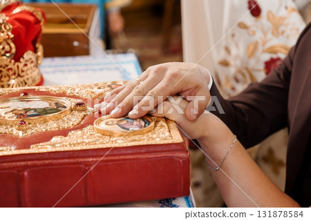Orthodox Wedding Ceremony: Hands Holding a Holy Book, Red and Gold Icons, Traditional Ritual, Faith, Love, and Marriage in Church Setting Orthodox Wedding Ceremony: Hands Holding a Holy Book, Red and Gold Icons, Traditional Ritual, Faith, Love, and Marriage in Church Setting 131878584