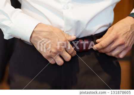 Man Fastening Dark Burgundy Leather Belt with Black Trousers. Close-up of Waist, Formal Attire, Professional Style, White Shirt, Indoor Shot 131878605