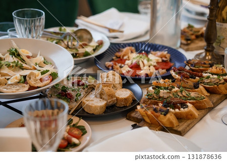 Appetizing Antipasto Table Spread Featuring Bruschetta, Salads, and Olives, Rustic Italian Cuisine, Dark Blue Plates, and White Linen. Appetizing Antipasto Table Spread Featuring Bruschetta, Salads, and Olives, Rustic Italian Cuisine, Dark Blue Plates, and White Linen. 131878636