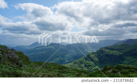 A view of rolling green hills and mountains, some with rocks on top, in the Gap of Dunloe in County Kerry, Ireland, under a cloudy sky during the day. A view of rolling green hills and mountains, some with rocks on top, in the Gap of Dunloe in County Kerry, Ireland, under a cloudy sky during the day. 131878682