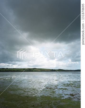A moody landscape with a cloudy sky over calm waters. A moody landscape with a cloudy sky over calm waters. 131878695