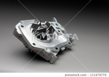 A new, shiny aluminum engine coolant pump on a gray gradient background. Contrast backlighting. A new, shiny aluminum engine coolant pump on a gray gradient background. Contrast backlighting. 131879778