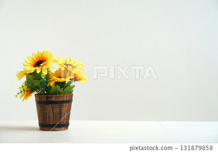artificial sunflower In a pot made from colored wood. Place the decorations on the white table. There is a blank white wall as the background for adding content. artificial sunflower In a pot made from colored wood. Place the decorations on the white table. There is a blank white wall as the background for adding content. 131879858
