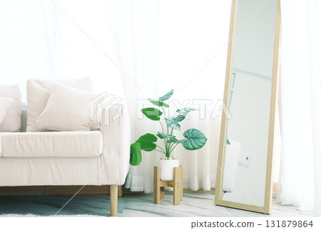 Simple white sofa With cloth pillows in the living room Decorated with green houseplants and a wooden framed mirror. Behind it is a translucent curtain. Natural light shines through making it bright 131879864