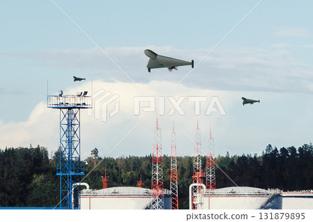 Military drones fly over the industrial area of the oil depot with antenna towers and a forest. 131879895