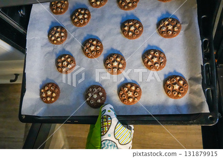 Top view photo of hand wearing oven mitt taking out hot tray with baked cookies from oven. Holiday cooking concept, homemade pastry, Christmas dessert preparation. Top view photo of hand wearing oven mitt taking out hot tray with baked cookies from oven. Holiday cooking concept, homemade pastry, Christmas dessert preparation. 131879915