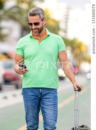 Traveler using phone. Tourist booking vacation trip. Traveler suitcase for summer trip. Man booking summer trip. Hispanic tourist traveler book online outdoor. Tourist with travel bag Traveler using phone. Tourist booking vacation trip. Traveler suitcase for summer trip. Man booking summer trip. Hispanic tourist traveler book online outdoor. Tourist with travel bag 131880079