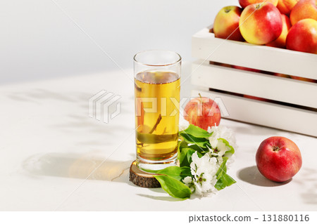 Apple juice. Full glass of natural apple juice on a wooden podium with red apples and blossom branche on a white table with copy space. Summer natural drink. Soft focus stile 131880116