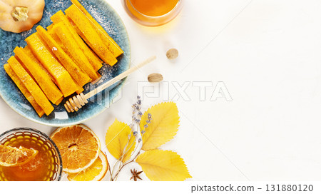 Baked pumpkin slices with cinnamon, honey and dried oranges with herbal tea on a white background with autumn leaves and copy space. Vegan dessert, healthy food. Autumn food. Flat lay 131880120