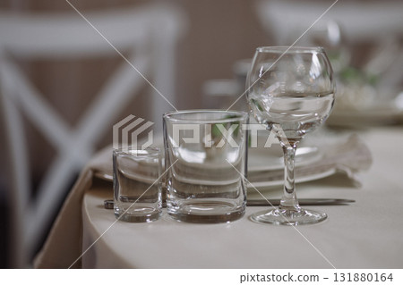 Empty glassware on elegant table with beige tablecloth and white chairs in soft light 131880164