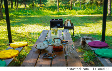 The summer breeze gently moves the tablecloth, while the tea set awaits guests for a delightful outdoor tea experience. 131880182