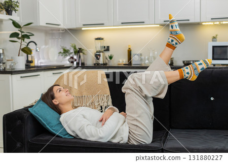 Young woman lies indoors enjoys leisure comfort laughs plays and waves legs with pure joy and fun 131880227