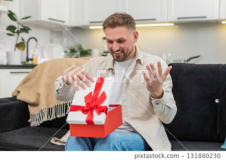 Young man lifts lid of gift box finds desired item freezes in surprise smiles with pure joy moment 131880230