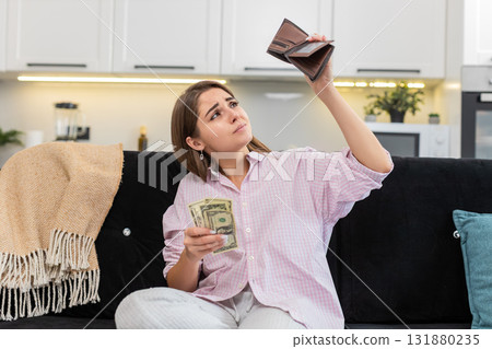 Young woman at home looks inside wallet sees small cash money dollars frowns about poverty debt 131880235