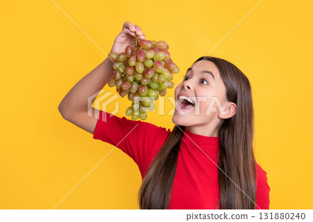 amazed child eat bunch of grapes on yellow background amazed child eat bunch of grapes on yellow background 131880240
