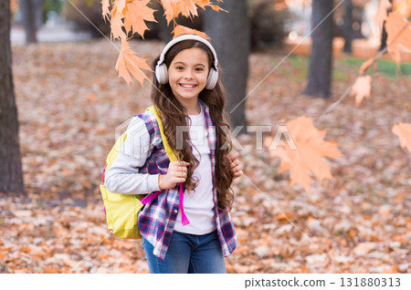 smiling child carry backpack and listen music, school time 131880313