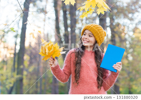Outdoor learning fun for the autumn months. Happy child hold book and autumn leaves. Back to school. Reading education. Knowledge day. Exploring and learning about nature in fall Outdoor learning fun for the autumn months. Happy child hold book and autumn leaves. Back to school. Reading education. Knowledge day. Exploring and learning about nature in fall 131880320