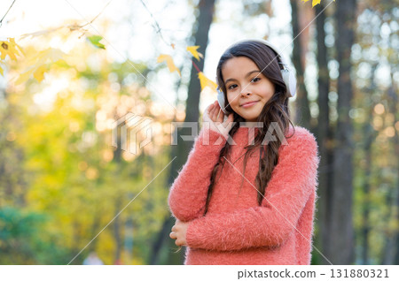 Confident in style. fall is a time for study. back to school. concept of online education. child in sweater enjoy listening ebook. new technology. girl in earphones. kid listen music in autumn park Confident in style. fall is a time for study. back to school. concept of online education. child in sweater enjoy listening ebook. new technology. girl in earphones. kid listen music in autumn park 131880321