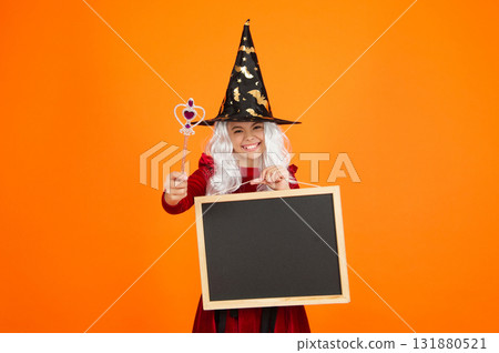 Girl in witch costume hold magic wand. Happy Halloween advertisement. Girl witch in Halloween costume isolated on orange. Halloween party advertisement. Hallows witch girl. Halloween sale Girl in witch costume hold magic wand. Happy Halloween advertisement. Girl witch in Halloween costume isolated on orange. Halloween party advertisement. Hallows witch girl. Halloween sale 131880521