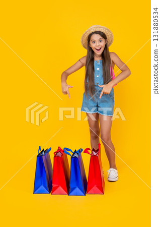 happy teen girl point finger on shopping bags on yellow background. full length 131880534