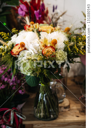 Autumn floral arrangement displayed in a clear glass vase on wooden surface. Seasonal bouquet design, cozy flower shop vibes, rustic natural decor, local florist craftsmanship 131880543