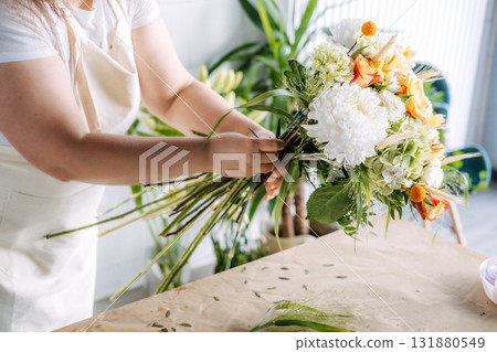 Florist tying stems of a handmade autumn bouquet on a craft table. Seasonal gifting, Thanksgiving florals, sustainable decor, creative expression Florist tying stems of a handmade autumn bouquet on a craft table. Seasonal gifting, Thanksgiving florals, sustainable decor, creative expression 131880549