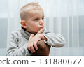 Thoughtful boy rests chin on knee, looking aside in a quiet indoor portrait contemplative childhood mood 131880672