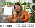 Middle-aged woman with genuine smile lighting up her face deeply engrossed in physical book at home 131881322