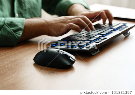 Person typing on a modern keyboard while using a computer mouse at a wooden desk 131881397
