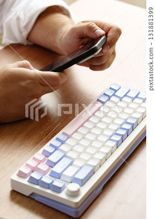 Individual using a smartphone while seated at a wooden table with a colorful keyboard 131881399