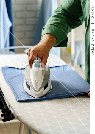 Ironing clothes at home with focus on a garment and an iron during a weekend morning Ironing clothes at home with focus on a garment and an iron during a weekend morning 131881452